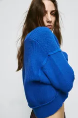 Jersey de punto color azul eléctrico con escote en pico, manga larga y detalle de costuras marcadas en los hombros. Presenta un corte ligeramente cropped con puños y ruedo acanalados.
