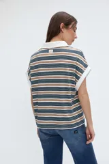 Musculosa tipo polo a rayas horizontales en tonos verdes, azules y blancos, con cuello y ribetes en contraste. Presenta media cartera de botones y tajos laterales en el dobladillo.