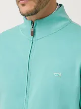 Buzo de algodón pima con cierre frontal completo, cuello alto y bolsillos laterales. Presenta un pequeño logo bordado en el pecho y detalles en contraste en el interior del cuello.