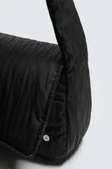 Bolso de hombro confeccionado en tejido técnico acolchado de color negro. Presenta un diseño de solapa con cierre magnético y cremallera, asa de hombro integrada y compartimentos interiores.
