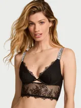 Bralette longline de encaje negro sin forro con aros, escote en V pronunciado, aberturas entrecruzadas en el centro y tirantes brillantes con logo de pedrería.