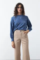 Pantalón ancho de tiro alto y corte recto, color marfil, con bolsillos frontales aplicados y cierre de doble botón metálico.
