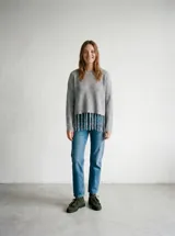 Buzo de punto gris jaspeado, de calce relajado, con cuello redondo, mangas largas y detalle de flecos en el ruedo delantero.