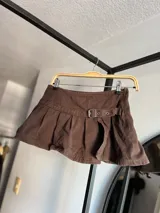 Minifalda de tiro bajo confeccionada en denim negro, con diseño plisado y detalle de hebilla frontal. Presenta un tajo lateral que aporta un estilo moderno y audaz.