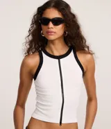 Musculosa blanca sin mangas de tejido seamless con cremallera frontal vertical y ribetes negros en contraste en el cuello y las sisas.