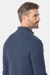 Buzo tejido de hombre color azul, con cuello alto y medio cierre frontal. Presenta una textura estructurada y un pequeño detalle metálico en la parte trasera del cuello.