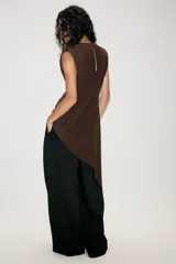 Vestido corto de color marrón, con cuello redondo y diseño sin mangas. Presenta un bajo asimétrico con un lateral más largo y cierre en la espalda con abertura y botón.