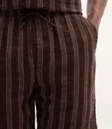 Bermuda masculina de corte recto confeccionada en tejido jacquard con textura y estampado de rayas verticales en tonos marrones. Cuenta con cintura elástica con cordón ajustable y bolsillos laterales.