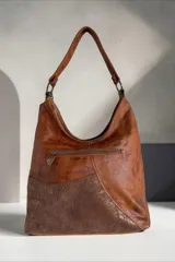 Cartera de cuero de diseño envolvente y líneas orgánicas, con combinación de texturas, apliques y estampado de serpiente, asa de hombro y bolsillos exteriores.
