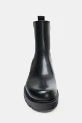 Botín Chelsea de caña media en color negro, con paneles elásticos laterales y tirador trasero. Presenta punta redonda y suela track robusta de 3 cm de altura.