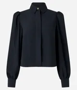 Camisa celeste de crepé con cuello inglés, manga larga abullonada y abotonadura frontal.