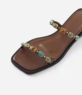 Sandalias planas estilo mule marrones, confeccionadas en PU, con diseño de dedo, dos tiras finas decoradas con aplicaciones de resina y detalles metálicos dorados.