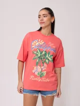 Remera color salmón con estampado de palmeras, flores y texto "California Ride the Tide Rusty Tribe".