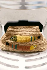 Bolso de mano tipo clutch confeccionado en rafia color beige con asa de madera oscura y cierre a presión. Decorado con dos peces bordados con cuentas y rafia de colores amarillo, marrón y verde.