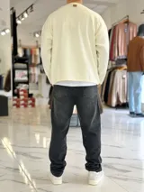 Sweater de punto liviano color beige, con textura marcada, cuello redondo y mangas largas de corte relajado, con pequeño estampado tipográfico negro en el lateral inferior.