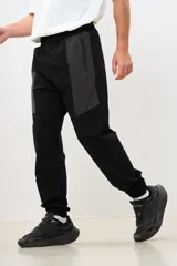 Pantalón de jogging negro con paneles grises en la parte superior, cintura elástica con cordón ajustable y puños elásticos en los tobillos.