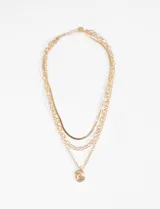 Collar de tres cadenas doradas superpuestas con dijes colgantes: una cadena de eslabones gruesos, una cadena de eslabones más finos y una cadena tipo serpiente. Incluye un dije ovalado con relieve de un racimo o sol.