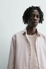 Camisa slim fit de algodón, color beige con rayas verticales blancas. Presenta cuello italiano, manga larga con puño de botón y cierre frontal de botonadura.