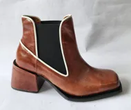 Bota tipo chelsea de cuero color óxido, con elástico lateral negro y ribetes en color crema. Presenta un taco cuadrado robusto y punta cuadrada.