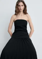 Vestido midi de fiesta con diseño combinado, cuerpo estilo palabra de honor en color negro y falda plisada evasé. Cuenta con cierre de cremallera lateral y forro interior.