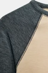 Camiseta de manga larga tipo ranglán con cuello redondo. Presenta un diseño bicolor con cuerpo en tono beige y mangas en gris jaspeado, con bajo redondeado.
