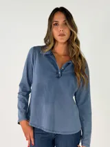 Remera de manga larga color azul, con cuello polo y cierre frontal parcial con botones. Presenta un corte holgado y un acabado suave.