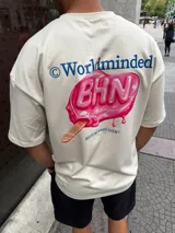 Remera de corte oversize color beige, con estampa gráfica en la espalda que representa un helado de palito derretido en color fucsia con la inscripción BHN y el texto Worldminded.
