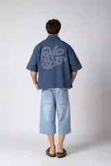 Camisa de manga corta negra 100% algodón, con calce boxy, cuello camisero, cierre frontal con botones y detalle de bordado blanco en la parte inferior.