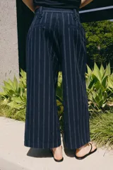 Pantalón de tiro medio confeccionado en mezcla de lino, con diseño de rayas verticales. Presenta cintura con trabillas, bolsillos laterales, pinzas en el delantero y cierre frontal con cremallera y botón.