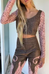 Pantalón de tiro alto y corte oxford confeccionado en cuero y encaje color negro. Presenta paneles de cuero en la parte superior con botones frontales y piernas de encaje transparente con diseño acampanado.