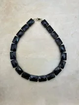 Collar corto de piedras facetadas rectangulares en rojo, blanco, negro y turquesa, con detalles dorados.