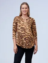 Blusa de seda fría con estampado animal print en tonos marrones. Tiene cuello redondo con escote en V y aro metálico decorativo.