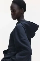 Canguro negro con capucha de doble capa, hombros caídos, bolsillo canguro y puños y bajo acanalados. Interior cepillado suave.