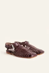 Sandalias planas tipo huarache de cuero negro, con tiras entrelazadas a mano y tira ajustable en el talón con hebilla metálica.