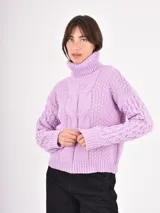 Polera de tejido de punto color lila, con cuello alto doblado y diseño de trenzas en el frente y las mangas. Presenta puños y ruedo acanalados.