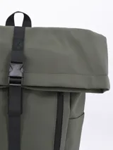 Mochila de estilo roll-top color verde oliva, con cierre principal ajustable mediante correa negra y hebilla de plástico. Presenta un bolsillo frontal con cierre vertical y base reforzada en color negro.