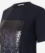 Remera negra de algodón con corte slim, cuello redondo y mangas cortas. Presenta un bloque rectangular frontal con lentejuelas plateadas.