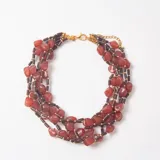 Collar de múltiples hilos con cuentas de piedra en tonos marrones y rojizos, intercaladas con pequeñas cuentas cilíndricas oscuras y detalles dorados. Cuenta con cierre de mosquetón y cadena de alargue dorada.