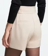 Bermuda roja de poliéster con cintura elástica, bolsillos laterales y cierre con cremallera y botones.