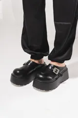Zuecos de plataforma alta estilo chunky, color negro, con diseño destalonado y una tira en el empeine con hebilla metálica plateada.