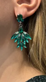 Caravanas colgantes con diseño de abanico, compuestas por cristales facetados en tonos verde esmeralda y detalles en color crema, con base metálica plateada.