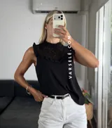 Blusa blanca sin mangas, de símil lino, con cuello alto y detalle de encaje calado y volados en el escote.