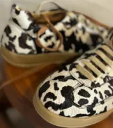 Zapatillas bajas con estampado de vaca en blanco y negro, con cordones marrones y suela de goma color miel.