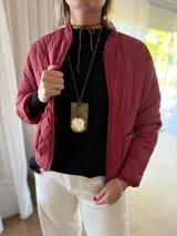 Campera tipo bomber acolchada con diseño de pespuntes ondulados, cierre frontal y bolsillos laterales con botón. Presenta un corte moderno y acabado en color bordo.
