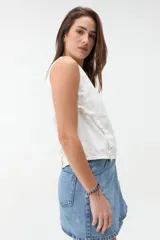 Blusa de denim blanco sin mangas, con cuello redondo y volados a lo largo de las costuras laterales.