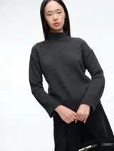 Sweater de tejido de punto en color gris oscuro, con cuello alto, mangas largas y puños acanalados. Presenta un diseño de corte recto y líneas simples.