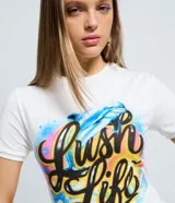 Remera de algodón con cuello redondo y mangas cortas. Presenta un estampado frontal con lettering 'Lush Life' y un delfín en estilo aerógrafo con colores vibrantes.