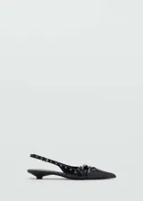 Zapato de charol negro con punta fina, escote asimétrico, tira trasera con hebilla ajustable y detalle de troquelado y apliques metálicos. Tacón kitten.