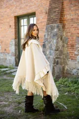 Ruana de tejido liviano color beige, con diseño abierto y detalles de volados en mezcla de lino y algodón. Presenta terminaciones con flecos en el ruedo y cordones decorativos con borlas en el frente.