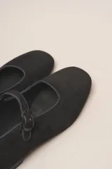 Zapato plano estilo Mary Jane de cuero negro, con punta fina y tira ajustable con hebilla sobre el empeine.